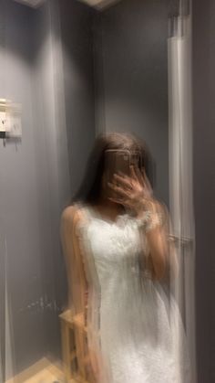 a blurry image of a woman in a white dress looking at her reflection in the mirror