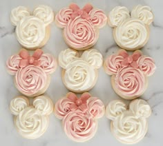 cupcakes with pink and white frosting shaped like mickey mouse heads on a marble surface