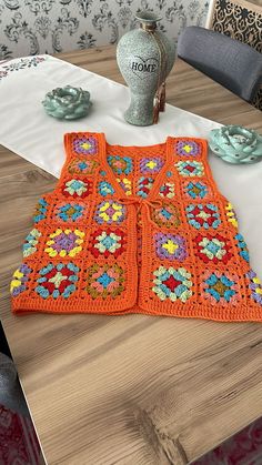 an orange crocheted sweater sitting on top of a table next to a vase