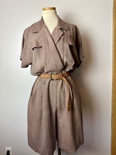 Women's romper or shorts style jumpsuit from the 1990's. It's a medium brown, made of a rayon fabric. Breast pockets are cosmetic only.  2 large pockets on the shorts half.  It is a blousy military style.  Unfortunately I do not have its original belt, so there is no belt included.  it has a nipped waist, with a zipper and the blouse crosses over with one button at the lapel/collar.  blouses over at waist.  It has a kind of marbled white wash creasing to the fabric. See all photos. I do not know what that's called or why. it seems intentional.  No stains, or tears. Looks good! no flaws.  Check measurements below.  ✏️✏️✏️DETAILS✏️✏️✏️ Brand: ALL THAT JAZZ Size on tag: (not todays size)  Fits like: large ish  Color:  pale brown Material: rayon Condition: very good Item includes: romper  (no Brown Short Sleeve Jumpsuits For Work, Vintage Summer Jumpsuits And Rompers For Work, Vintage Jumpsuits And Rompers For Summer Workwear, Brown Short Sleeve Jumpsuits And Rompers For Spring, Short Sleeve Khaki Jumpsuits And Rompers With Pockets, Khaki Short Sleeve Jumpsuits And Rompers With Pockets, Khaki Short Sleeve Jumpsuit With Pockets, Casual Brown Short Sleeve Jumpsuits And Rompers, Neutral Jumpsuit