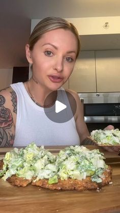 a woman standing in front of two pizzas on top of a wooden cutting board