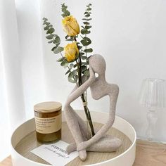 a vase with flowers in it and a statue on the table next to it that has a jar of honey