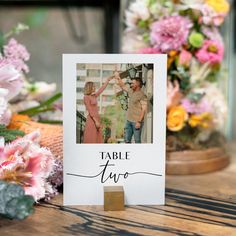 a table sign with two people holding each other's hands and flowers in the background