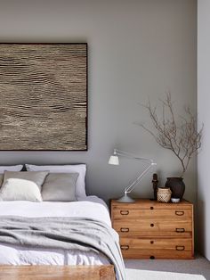 a bed sitting next to a wooden dresser under a painting on the side of a wall