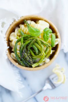 a wooden bowl filled with pasta and vegetables on top of a white cloth next to silverware