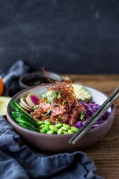 a bowl filled with salad and chopsticks on top of a wooden table