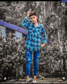 a young man is standing in front of some trees with his hand on his head