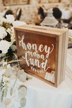 a sign that says honey moon fund sitting on top of a table with flowers and greenery