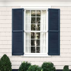 an open window with blue shutters on the side of a white brick building and potted plant in front