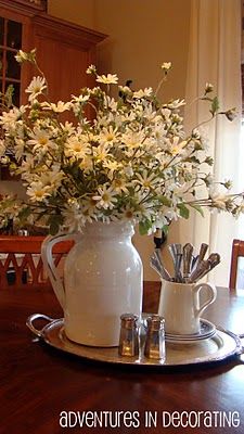 a white pitcher filled with flowers on top of a wooden table