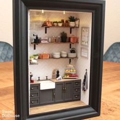 a miniature kitchen with shelves, sink and cabinets is shown in a shadow box on a table