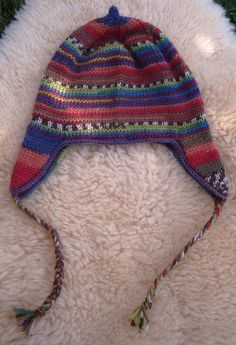 a multicolored knitted hat laying on top of a white furry surface with green grass in the background