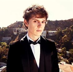 a young man in a tuxedo poses for a photo on top of a building