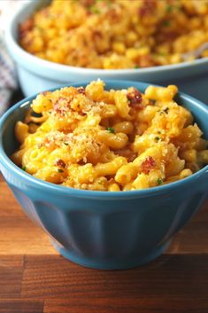 two blue bowls filled with macaroni and cheese on top of a wooden table