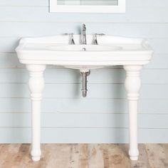 a white sink sitting on top of a wooden floor next to a framed picture above it