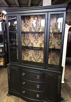 a black china cabinet with glass doors and ornate designs on the front, sitting in a warehouse