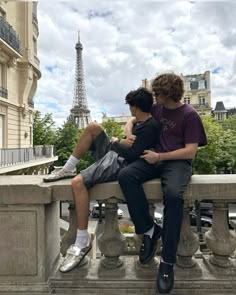 two young men sitting on a stone bench in front of the eiffel tower