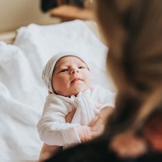 a baby laying on top of a white bed next to a woman's hand