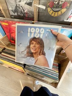 a person holding up a record album in front of a shelf full of vinyl records