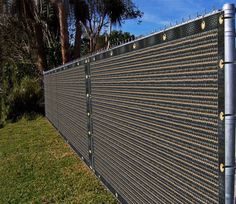 an image of a fence that has been installed on the side of a hill with grass and palm trees in the background