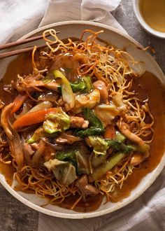 a white bowl filled with noodles and veggies next to a cup of tea