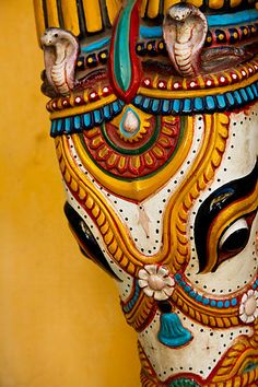 an intricately painted mask on display against a yellow wall