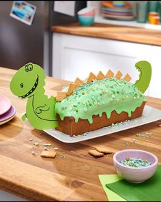 a dinosaur cake with sprinkles and green frosting on a table in a kitchen