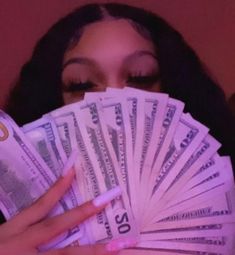 a woman hiding her face behind a fan of twenty dollar bills with one eye open