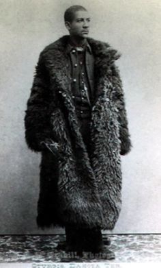 an old photo of a man wearing a fur coat and standing in front of a wall