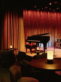 an empty stage with a piano, stools and table in front of red curtains