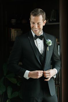 a man in a tuxedo smiles as he adjusts his bow tie