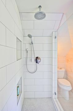 a white tiled bathroom with a shower head and hand held shower faucet next to the toilet