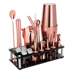 an assortment of rose gold colored metal items on a black tray with silver cups and spoons