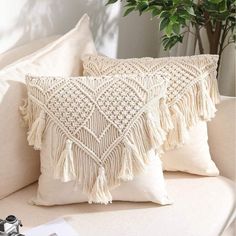 two white pillows with tassels are on a couch next to a potted plant