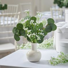 a vase filled with white flowers on top of a table next to other tables and chairs