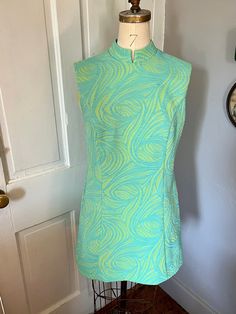 "This is a fantastic mini dress from the 1960s in the iconic mod silhouette, made by the brand Koret of California. Just imagine it with a pair of white go-go boots, or some colored leggings and platforms! The fabric seems to be a double-knit synthetic that has some stretch to it, with a raised aqua blue pattern on top of a sherbety lime green. There is a satin-like lining at the top near the collar and bust, but the rest of the dress is unlined. The dress is fitted at the waist then flares out, Green Fitted Vintage Mini Dress, Blue Fitted Mod Mini Dress, Retro Knee-length Lined Mini Dress, Vintage Blue Knee-length Mini Dress, Blue Sleeveless Retro Mini Dress, Vintage Blue Mini Dress, Blue Retro Sleeveless Mini Dress, Retro Blue Sleeveless Mini Dress, Vintage Fitted Blue Mini Dress