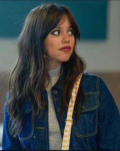 a woman with long hair wearing a denim jacket and holding a yellow striped bag in her hand