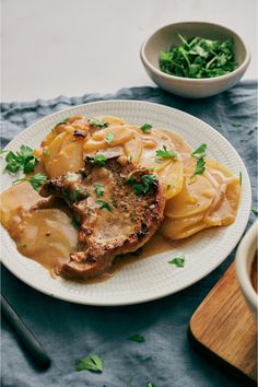 a white plate topped with meat covered in gravy next to a bowl of greens