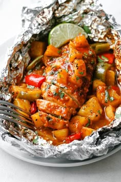 a close up of a plate of food with chicken and vegetables in foil on it