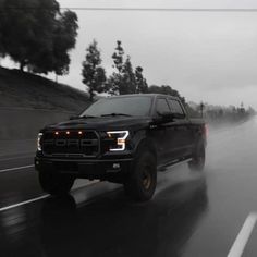 a black truck driving down a wet road