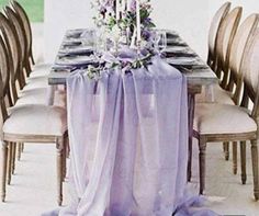 the table is set with purple linens and candles on it, along with white chairs