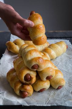 a person reaching for a hot dog wrapped in dough on top of some croissants