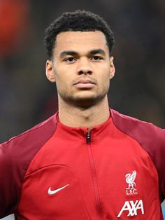 a close up of a soccer player wearing a red shirt and black pants with his hands on his hips