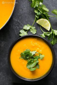 a bowl of carrot soup with cilantro and lime garnish on the side