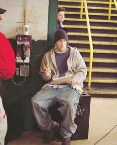 two men sitting next to each other in front of a pay phone and telephone booth