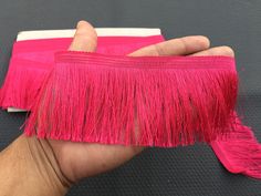 a hand holding a pink piece of cloth with fringes on it's end