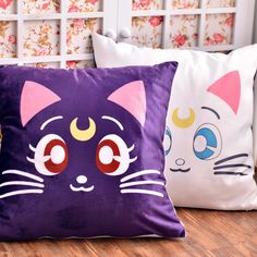 two decorative pillows with cats on them sitting on a wooden floor in front of a window