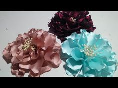 three different colored flowers on a white surface with pearls in the center and one pink, one blue