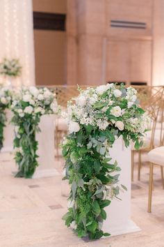 white flowers and greenery are arranged on pedestals at the end of an aisle