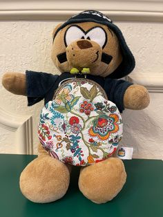 a stuffed animal holding a purse on top of a green table next to a white wall